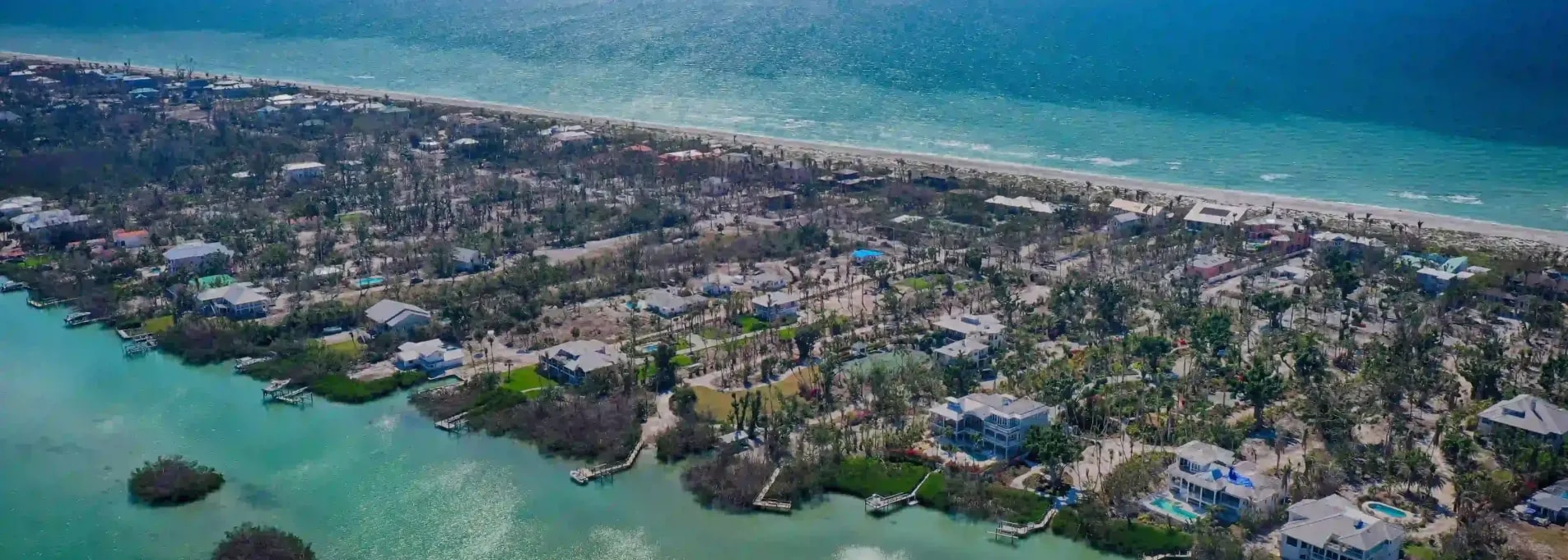 Aerial view of beachfront development with waterfront homes and dense vegetation along a coastal edge