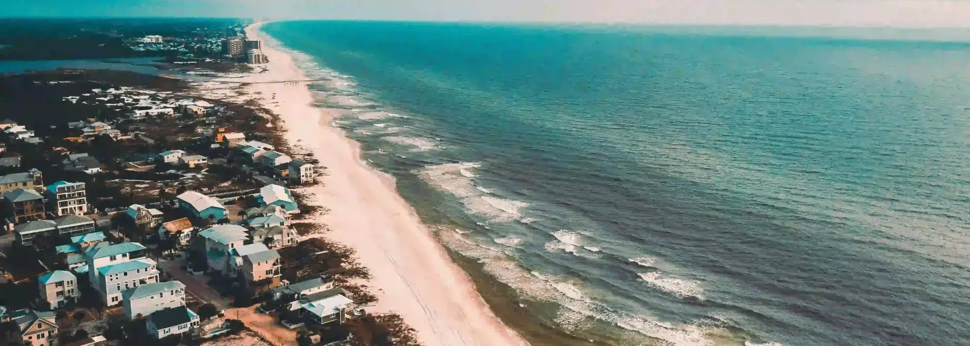 Drone shot of coastal homes along white-sand beach with turquoise waters and residential development