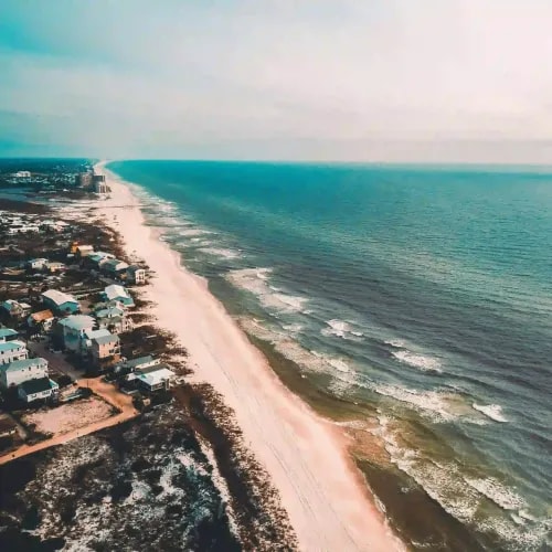 Drone shot of coastal homes along white-sand beach with turquoise waters and residential development