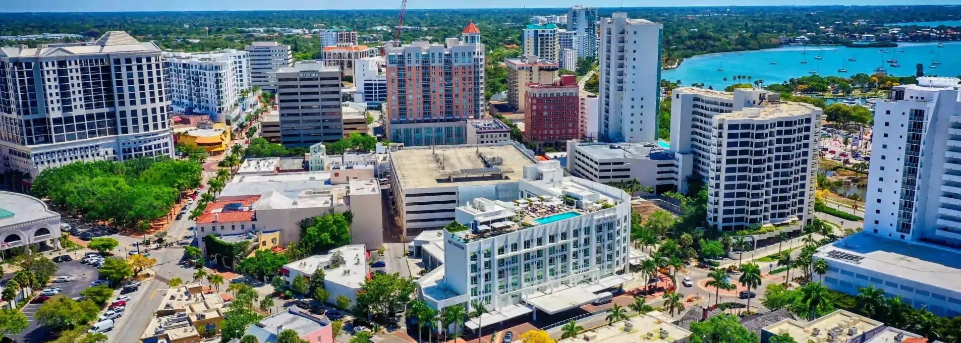 High-angle cityscape showcasing mid-rise and high-rise buildings near a bayfront with visible marina